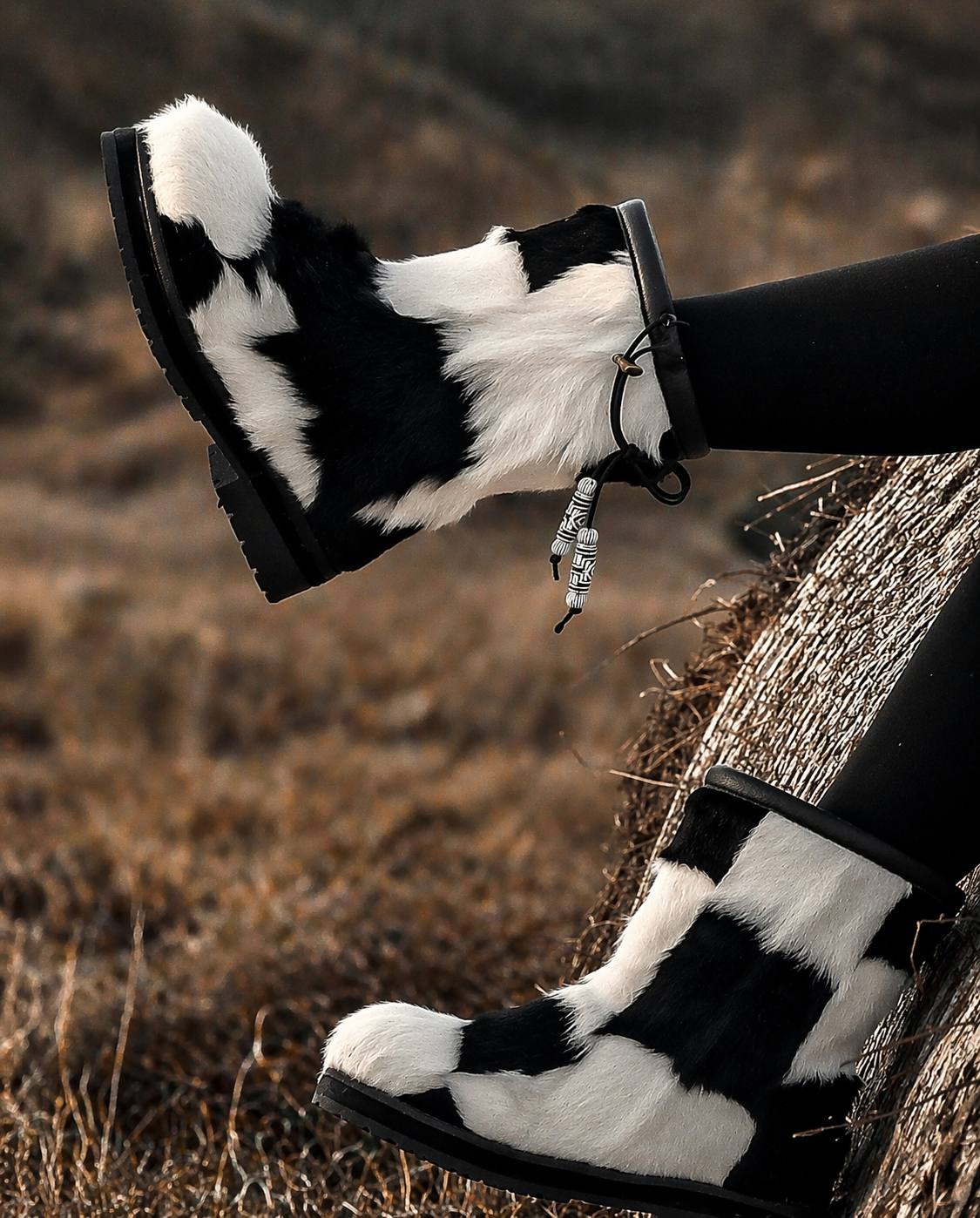 MOGSki handcrafted natural fur snow boots styled beside rustic log, luxury Mongolian winter footwear outdoor setting